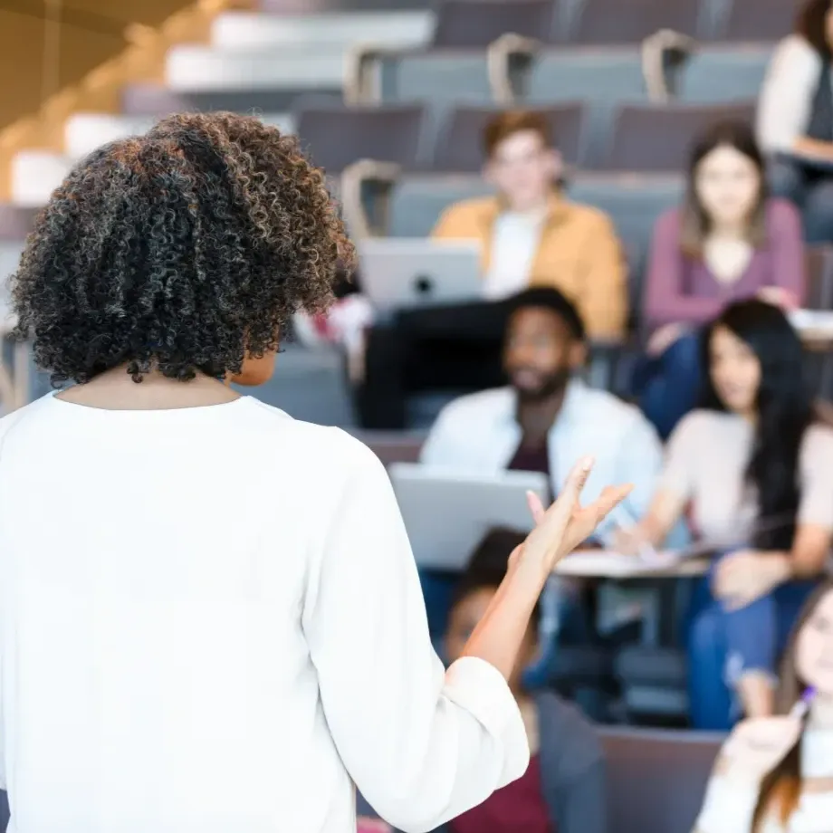 Presenter speaking to an audience in a lecture hall during a conference or educational session.