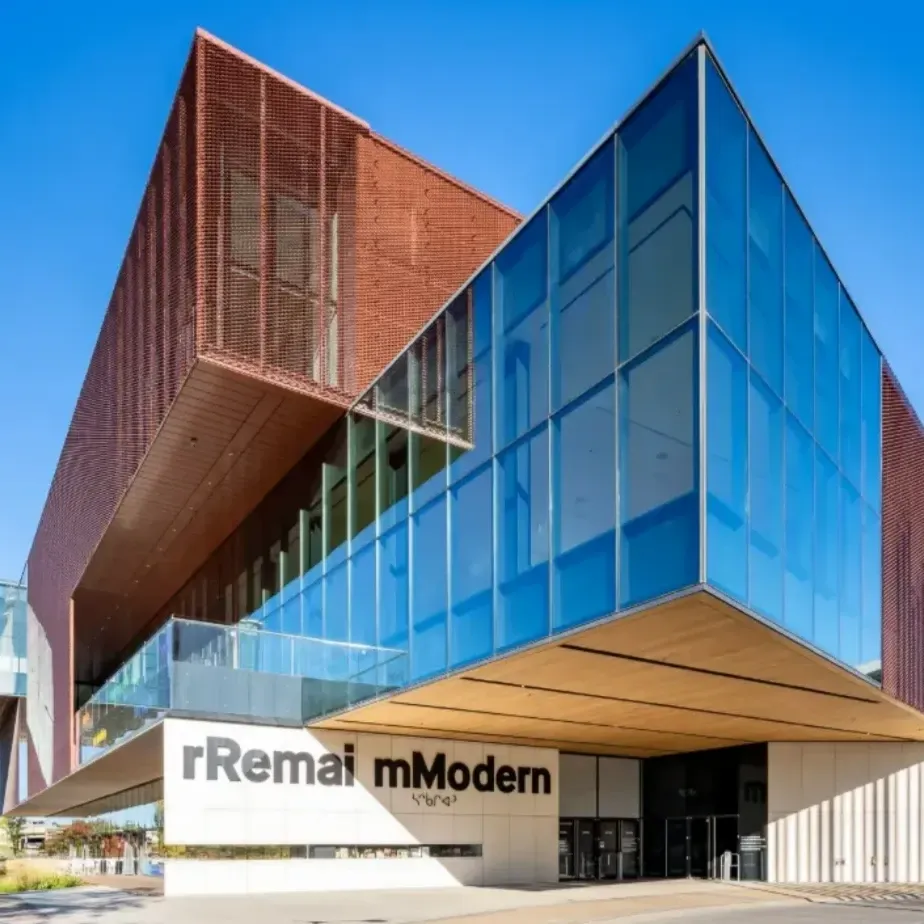 Exterior view of Remai Modern, a contemporary art museum with striking glass and weathered steel architecture under a clear blue sky.