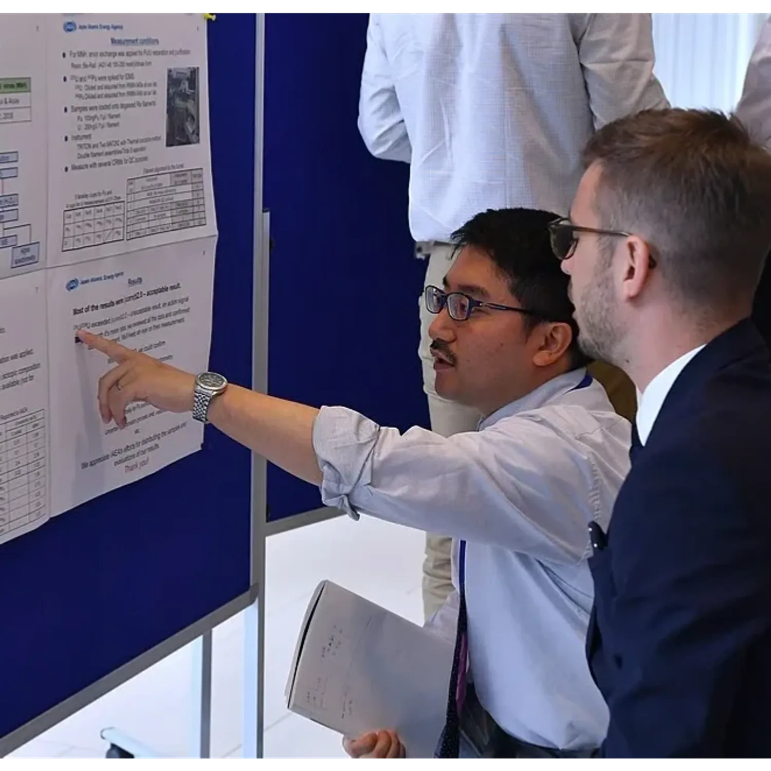 Two people looking at a conference poster, one pointing to text on the poster.