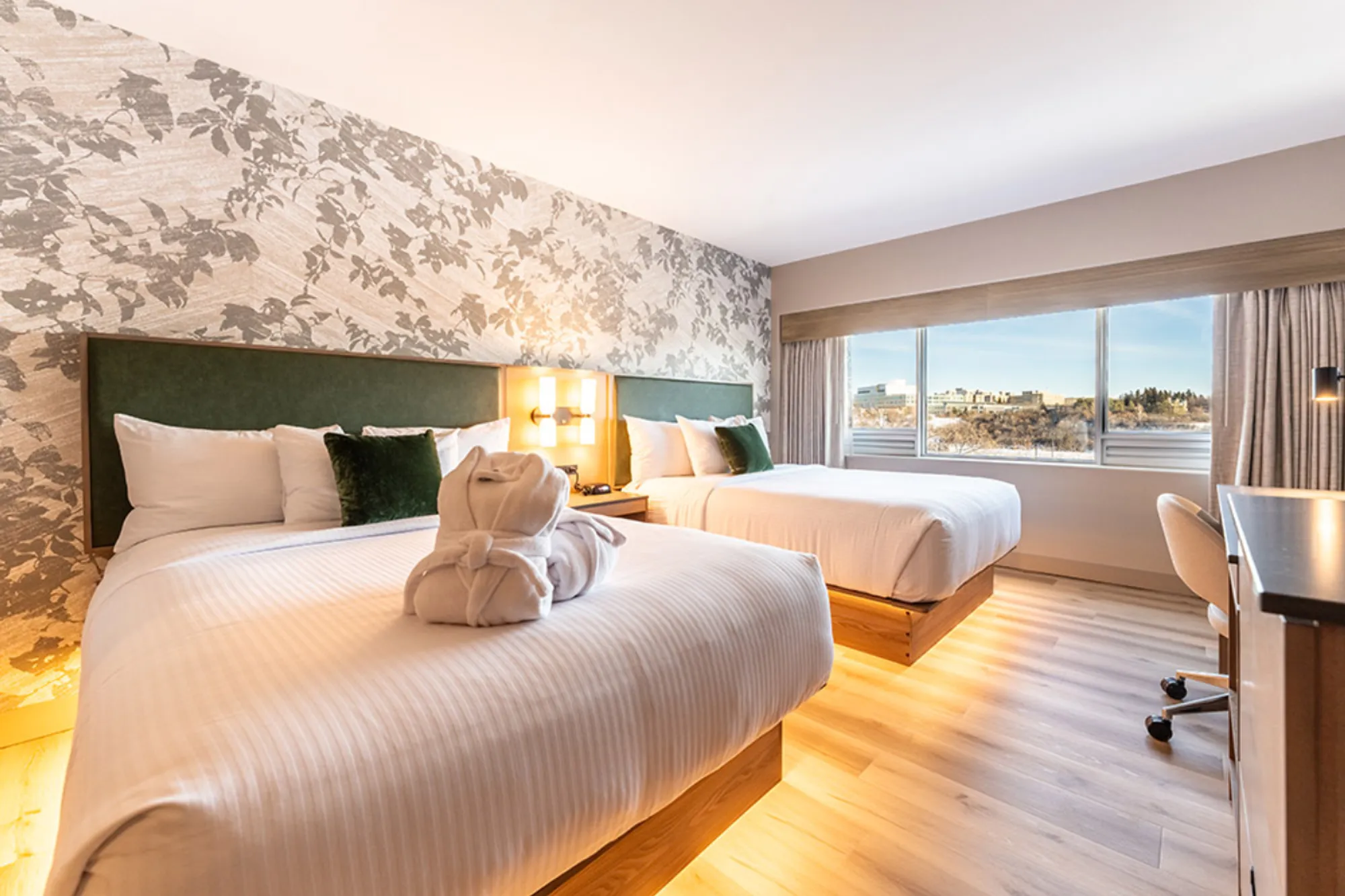 Modern hotel room with two queen beds, a work desk, and a large window overlooking the surrounding area.