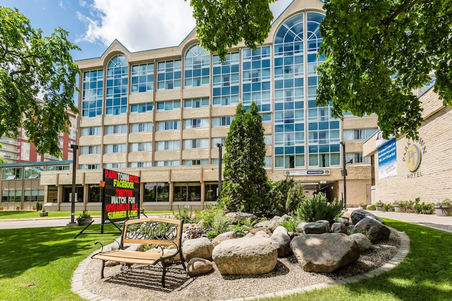 Exterior view of the Park Town Hotel, featuring a modern multi-storey building with landscaped gardens, trees, and the main entrance.