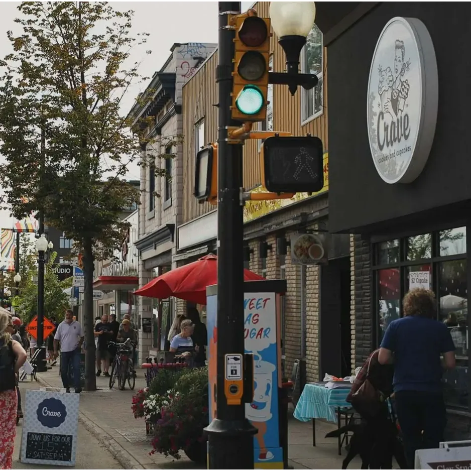 People stroll along Broadway Avenue in Saskatoon, with local shops, cafés, and a lively street market creating a vibrant neighbourhood atmosphere.