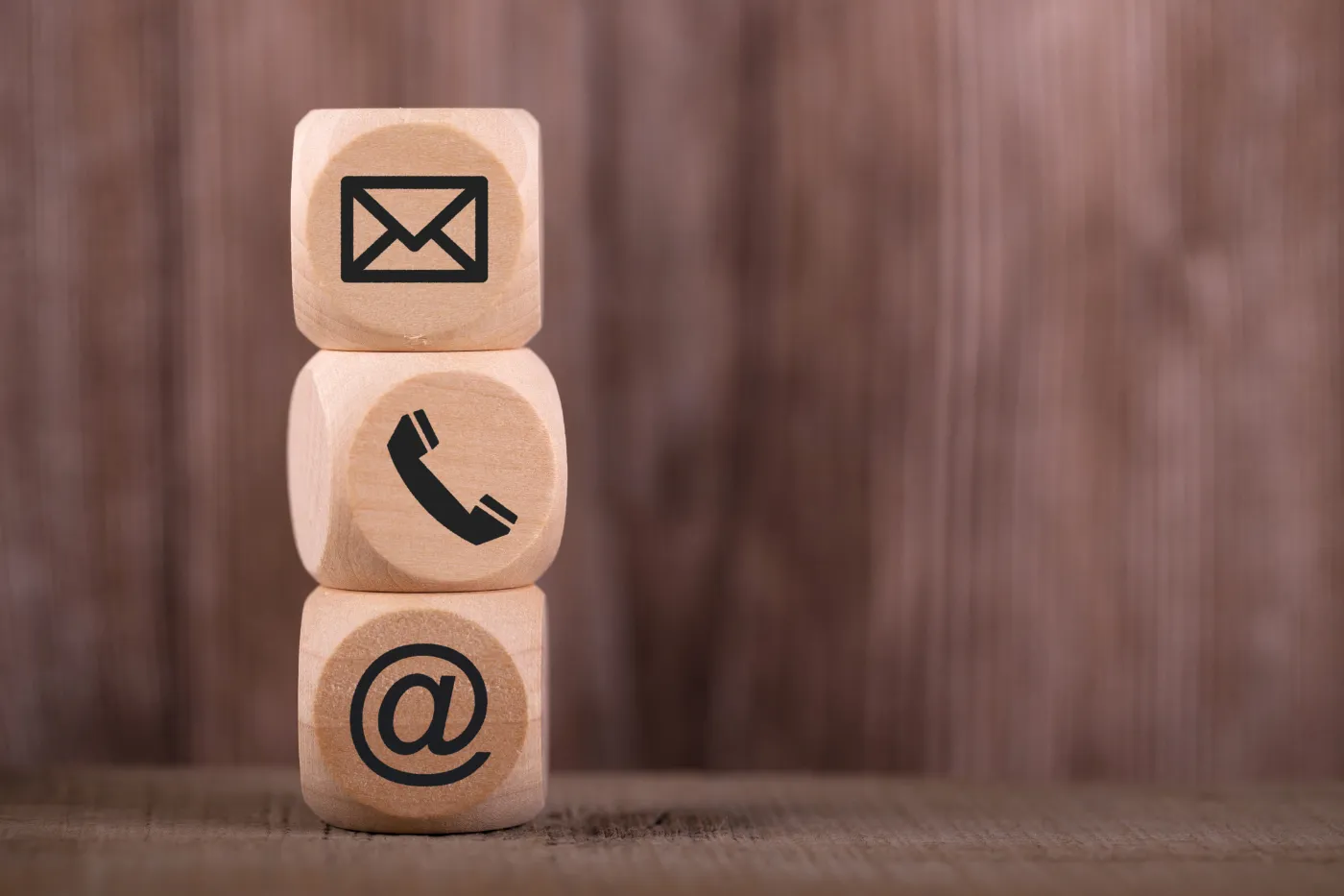 Wooden blocks displaying email, phone, and contact icons, representing communication and contact information.