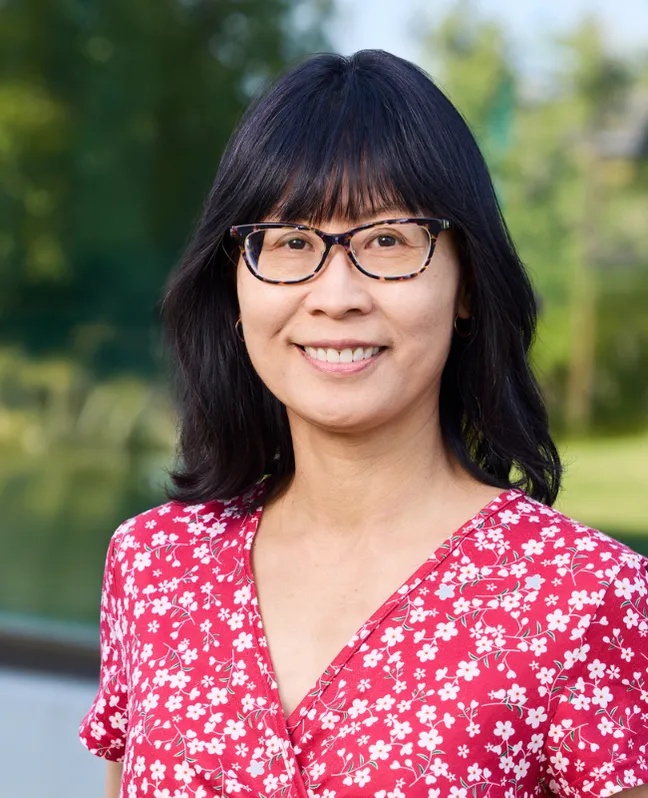 Professional headshot of a smiling woman wearing glasses with short black hair.