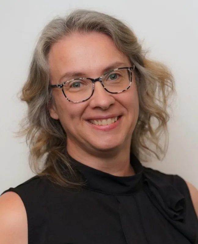 Headshot of Camille Lapierre smiling at the camera, wearing glasses and a sleeveless black top against a light grey background.